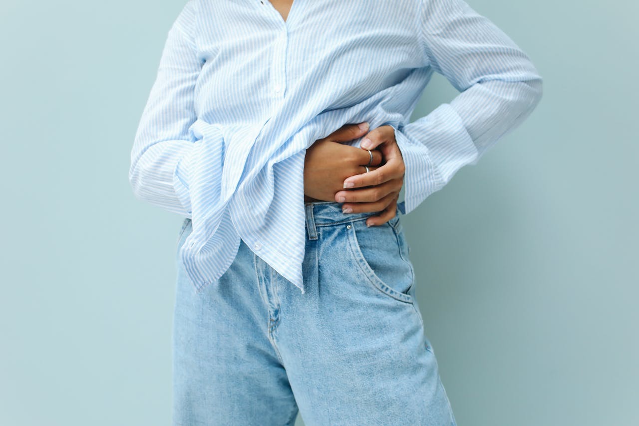 A person in a blue striped shirt and jeans, posing fashionably against a neutral background.